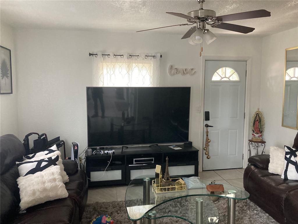 A living room features a large television, dark leather sofas, and a ceiling fan — 1803 SPRINGTIME AVENUE, CLEARWATER, FL