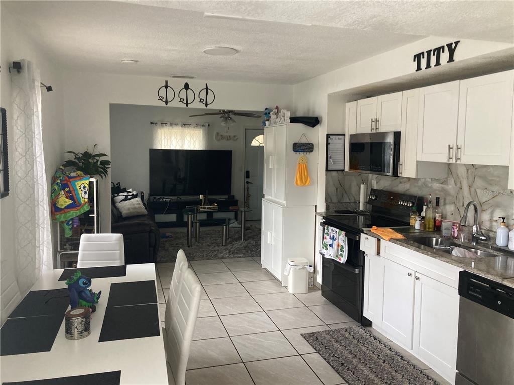 A kitchen with white cabinets and black appliances opens into a living room with tile floors — 1803 SPRINGTIME AVENUE, CLEARWATER, FL