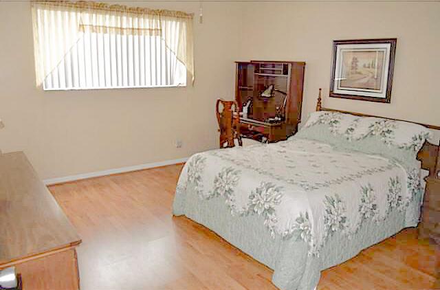 A bedroom with light wood flooring, a bed with a floral quilt, and a desk — 2100 NE 38th Street # 141, Lighthouse Point FL 33064, LIGHTHOUSE POINT, FL