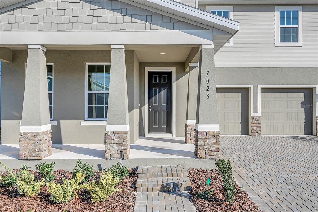 A gray house exterior features a covered porch, stone-based columns, and a paved driveway — 7023 KIWANO WAY, WINDERMERE, FL