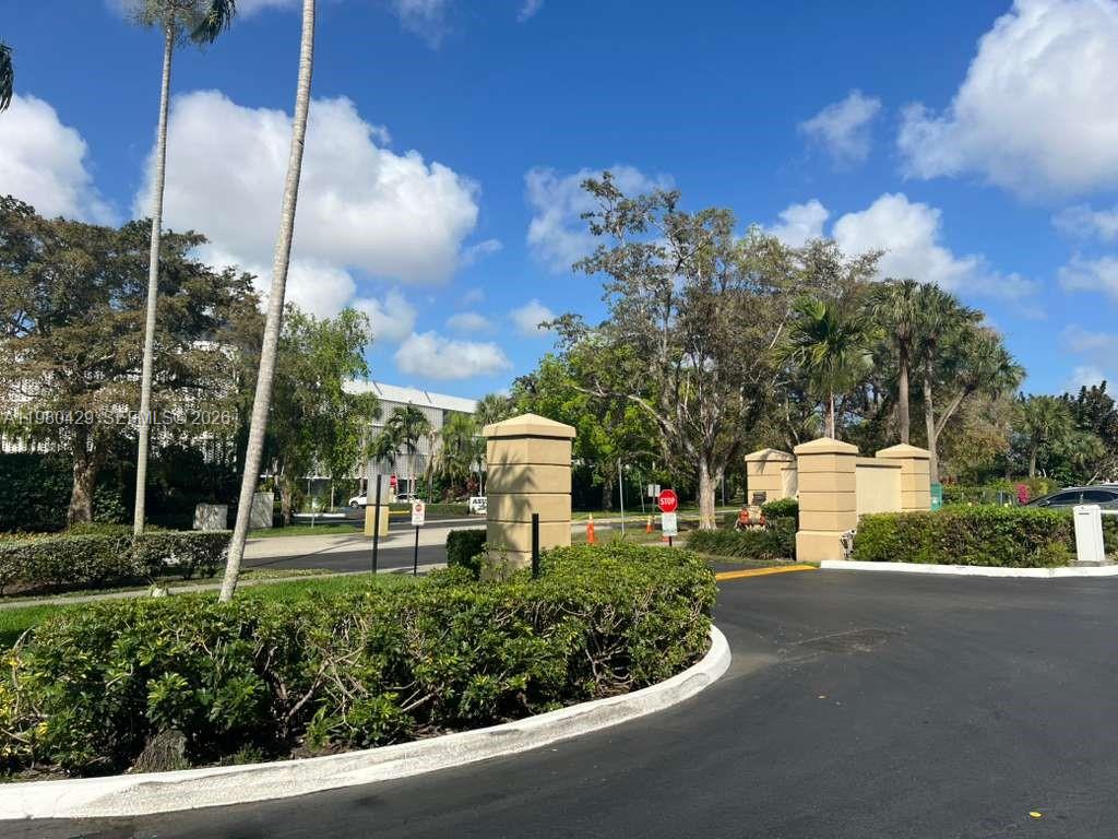 A paved driveway leads to a gated entrance with stone pillars and lush landscaping — 800 NE 195th St # 501, Miami FL 33179, MIAMI, FL