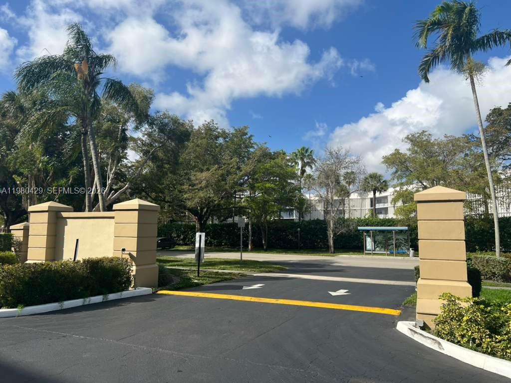 An entrance gate with two tan pillars leads to a paved driveway and trees — 800 NE 195th St # 501, Miami FL 33179, MIAMI, FL