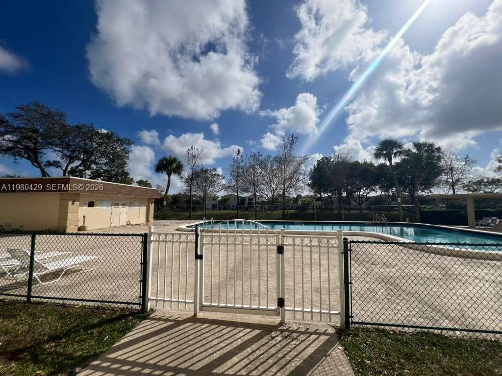 A gated community swimming pool area features a tan building and surrounding palm trees — 800 NE 195th St # 501, Miami FL 33179, MIAMI, FL