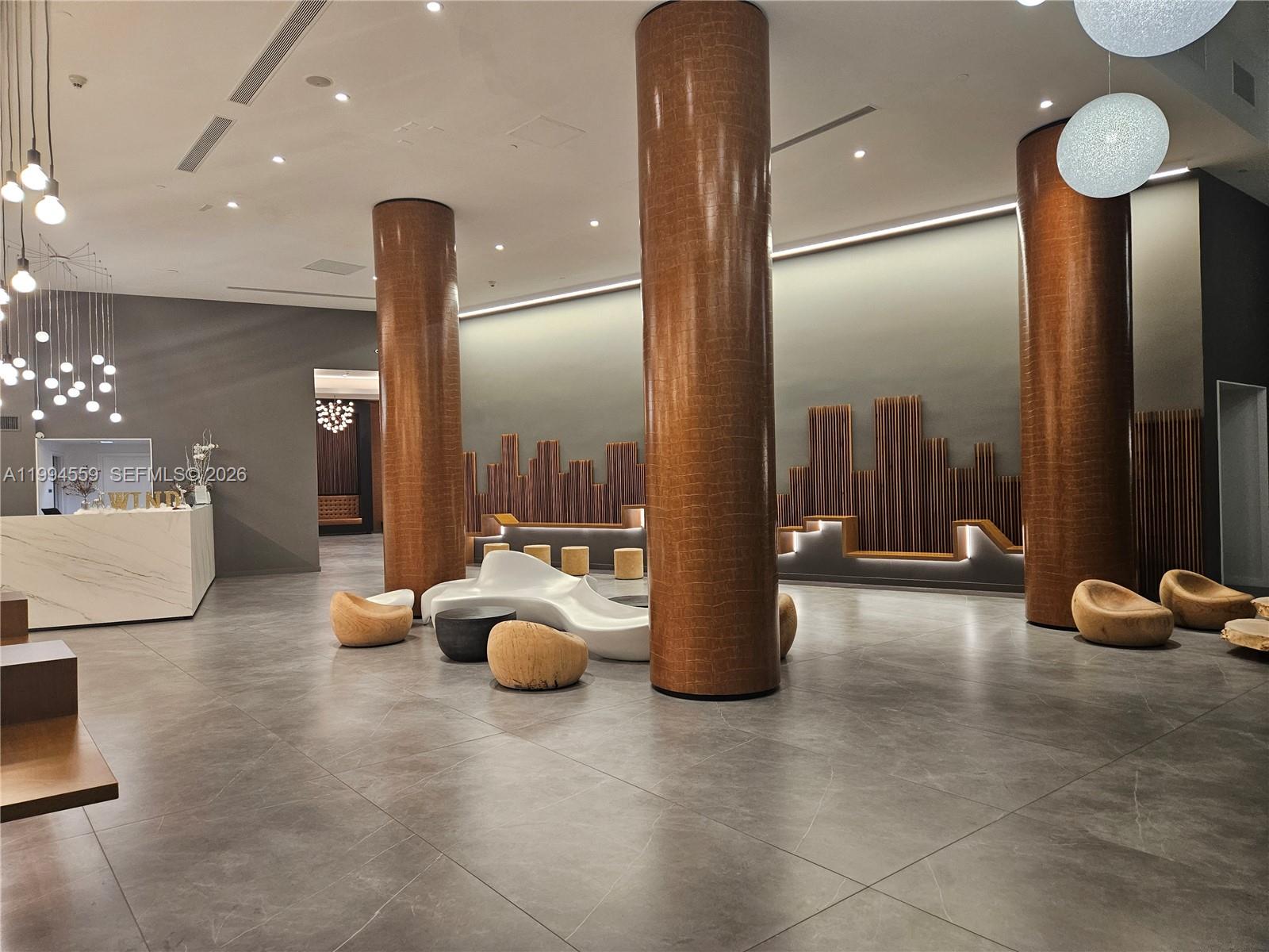 A modern lobby features large brown columns, gray tile flooring, and sculptural white seating — 350 S Miami Ave # 2714, Miami FL 33130, MIAMI, FL