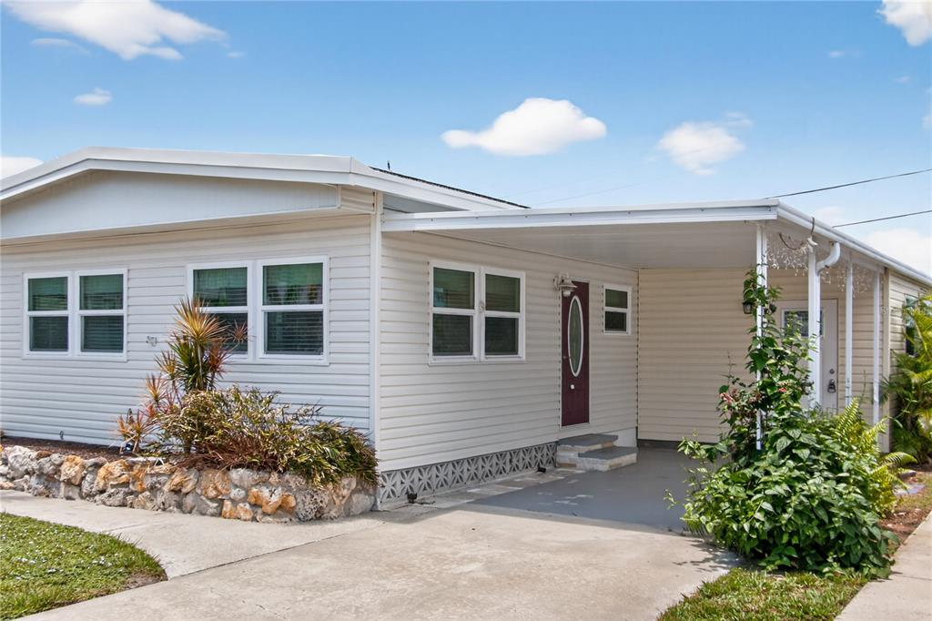 A single-story manufactured home with light siding, a covered carport, and a stone garden bed — 808 S GREEN CIRCLE, VENICE, FL