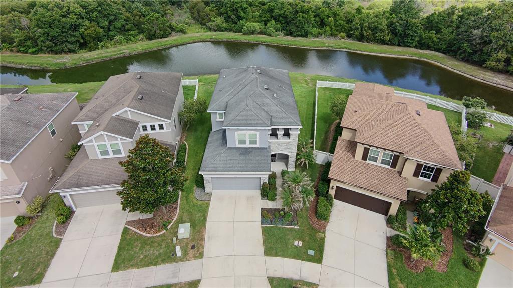An aerial view shows three suburban houses with driveways and backyards bordering a small pond — 7651 WINDCHASE WAY, WESLEY CHAPEL, FL