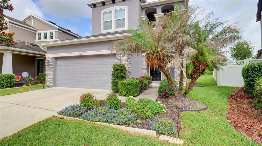 A two-story house with a gray garage, stone accents, and a palm tree in front — 7651 WINDCHASE WAY, WESLEY CHAPEL, FL