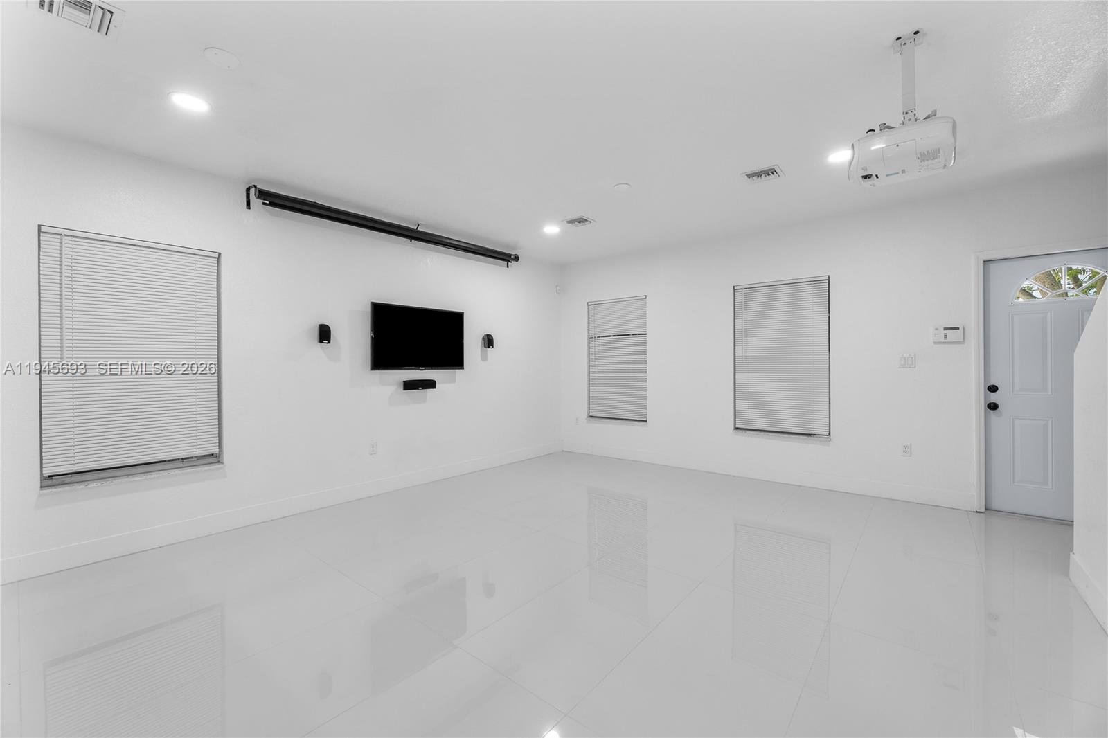 A bright, empty room features white walls, glossy tile floors, a wall-mounted television, and a projector — 1541 NW 1st Ct, Miami FL 33136, MIAMI, FL