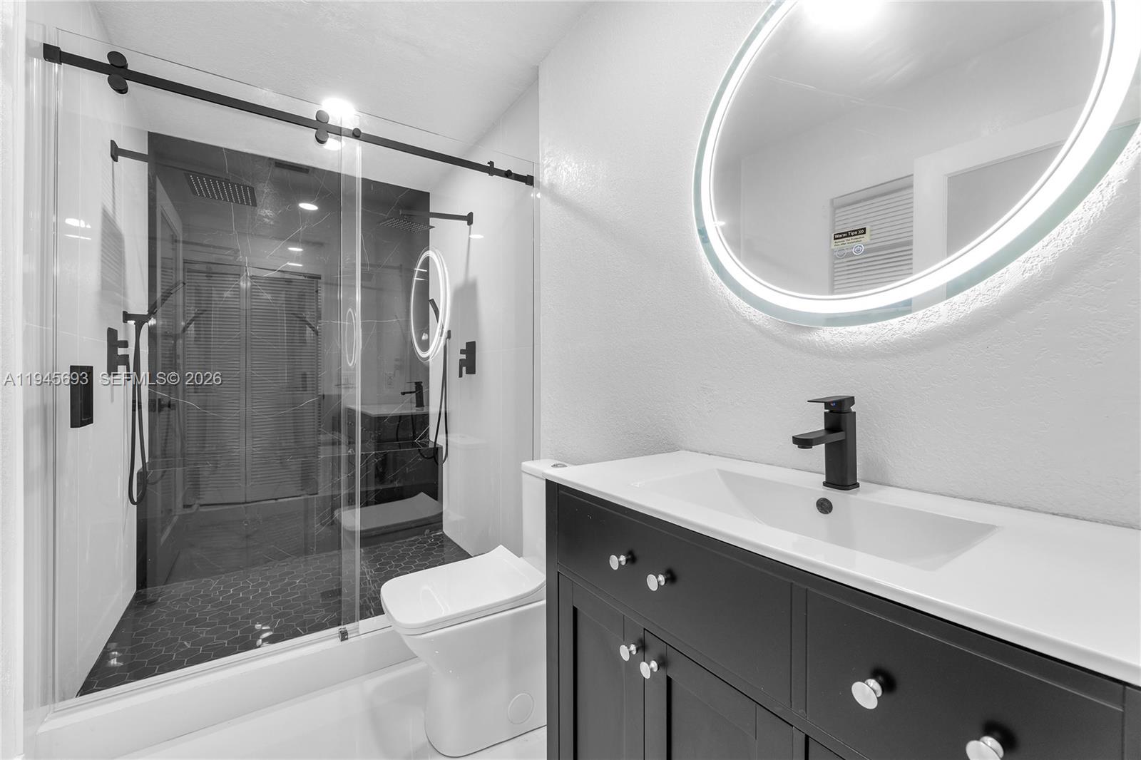 A modern bathroom features a black vanity, a round LED mirror, and a glass-enclosed shower — 1541 NW 1st Ct, Miami FL 33136, MIAMI, FL
