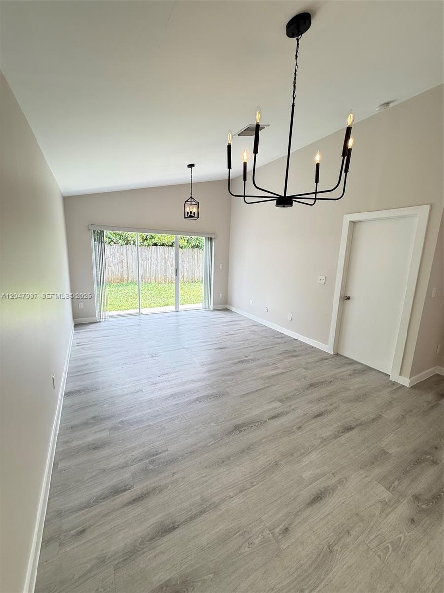 An empty room features light wood-look flooring, a vaulted ceiling, and two hanging light fixtures — 10113 SW 223rd Ter, Cutler Bay FL 33190, CUTLER BAY, FL