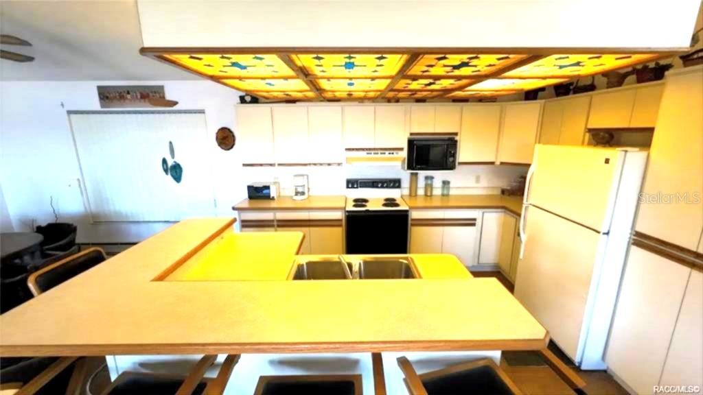A kitchen features light-colored cabinets, a yellow countertop, and a large, illuminated drop ceiling — 5340 BLOUNT ISLAND, HOMOSASSA, FL