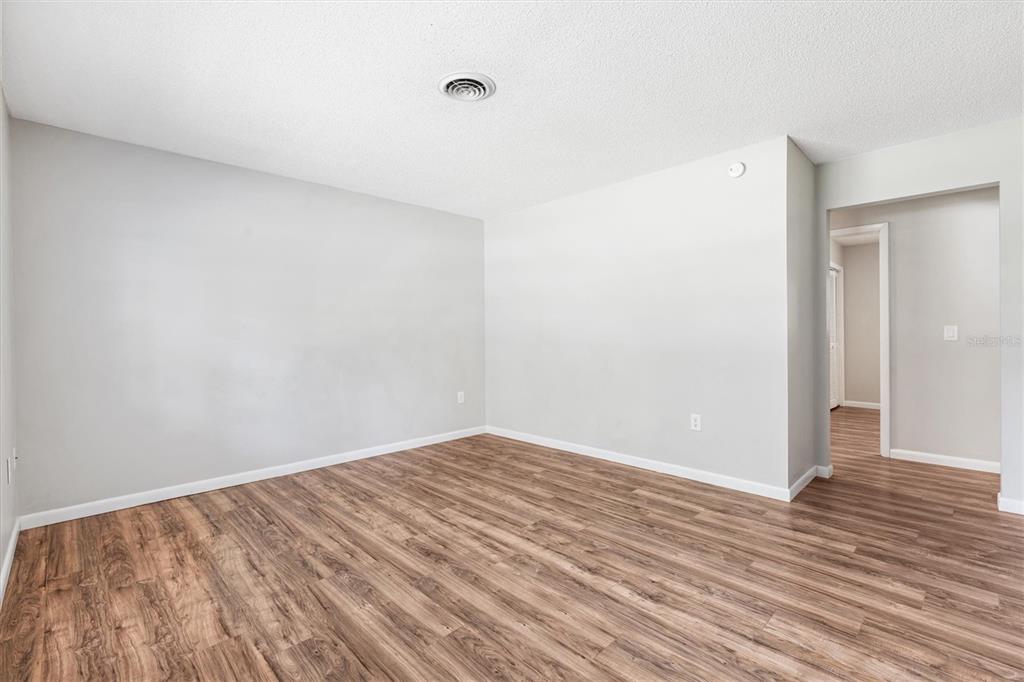 An empty room features light gray walls, wood-look flooring, and a circular ceiling vent — 603 MILRAY DRIVE, WILDWOOD, FL