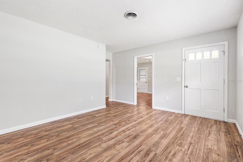 An empty room with light gray walls, wood-look flooring, and a white front door — 603 MILRAY DRIVE, WILDWOOD, FL