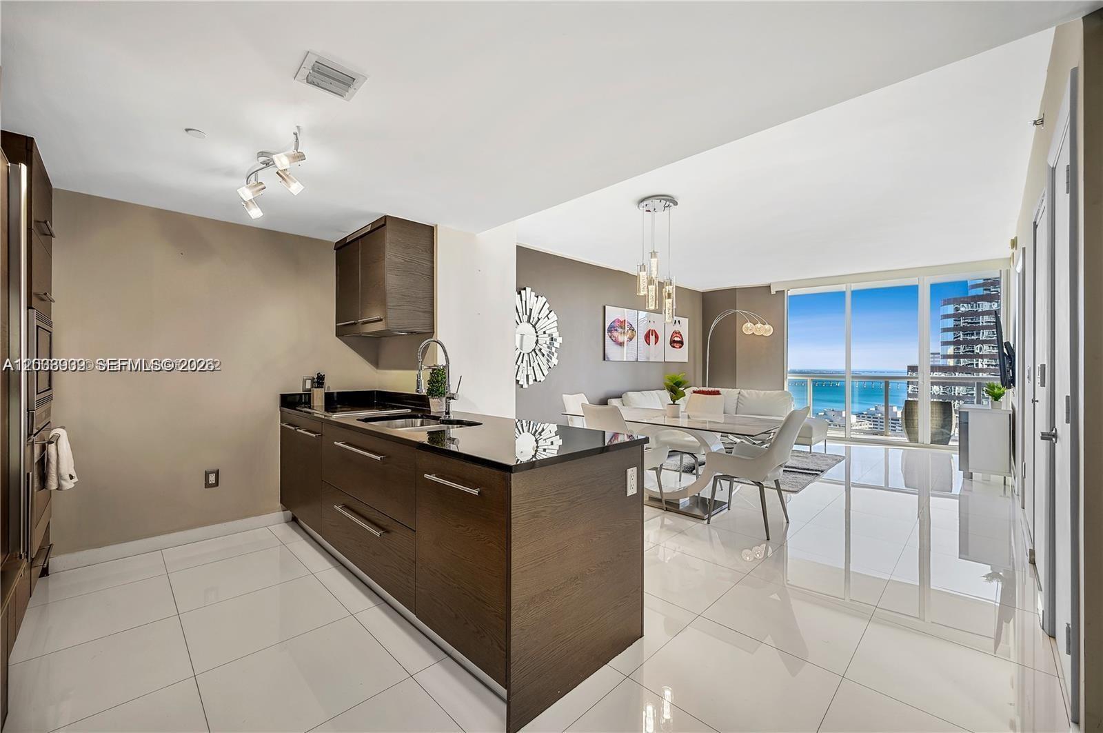 A modern kitchen with dark wood cabinets and black countertops opens into a dining area — 485 Brickell Ave # 3109, Miami FL 33131, MIAMI, FL