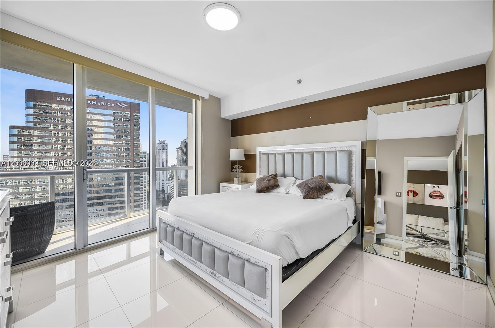 A modern bedroom features a white upholstered bed, glossy tile floors, and floor-to-ceiling windows — 485 Brickell Ave # 3109, Miami FL 33131, MIAMI, FL