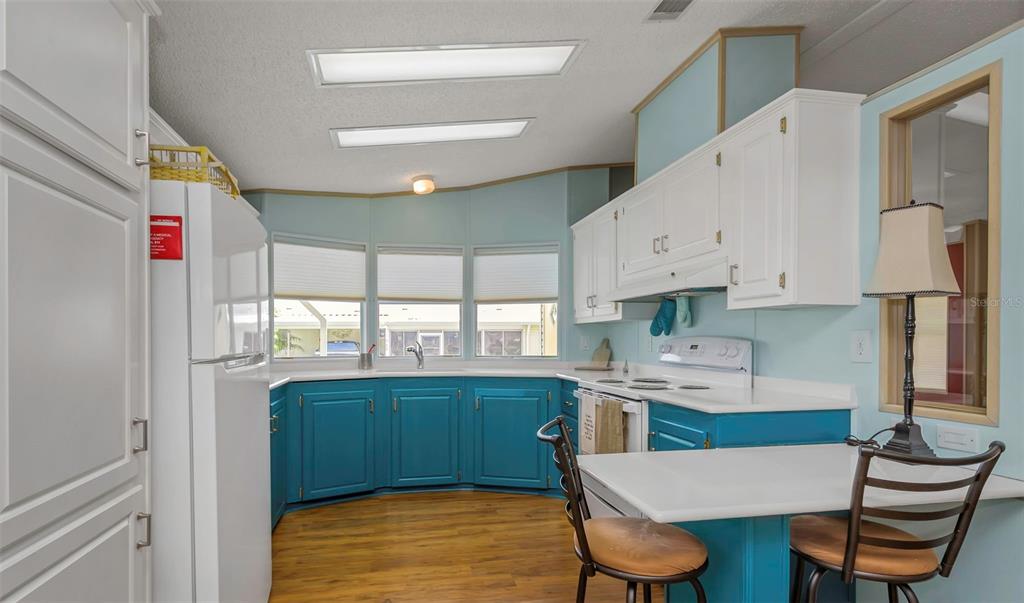 A kitchen features blue lower cabinets, white upper cabinets, white countertops, and a breakfast bar — 106 THATCH PALM STREET W, LARGO, FL