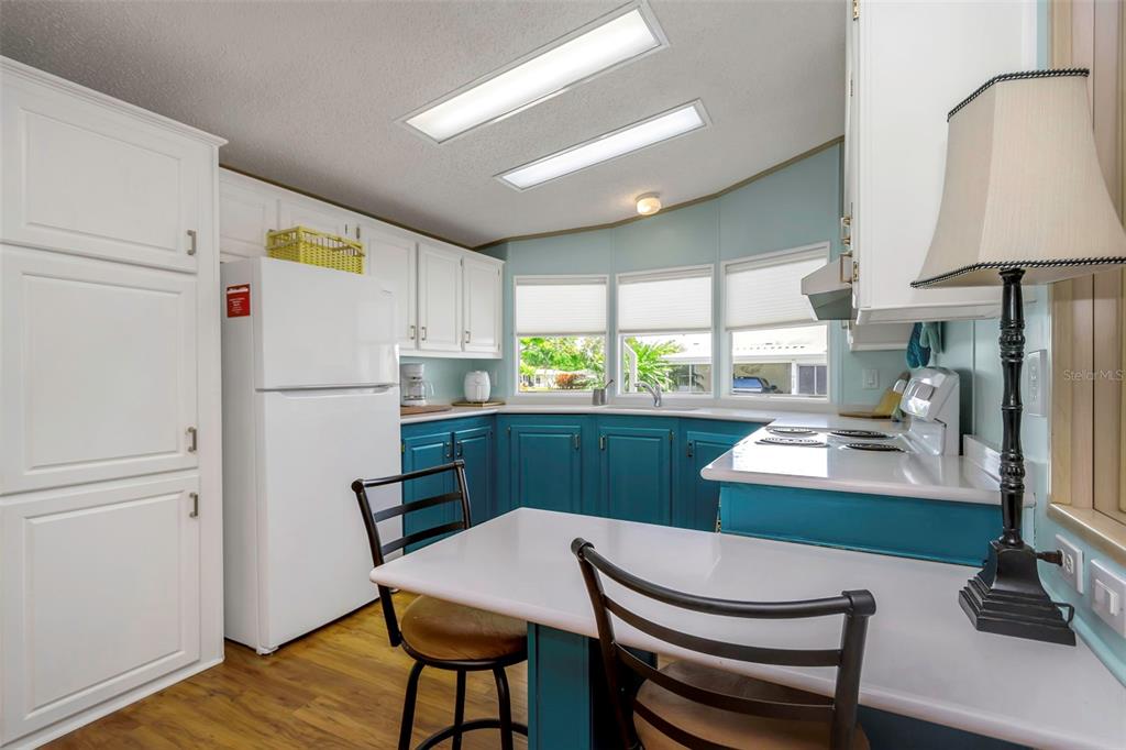 A kitchen features white upper cabinets, teal lower cabinets, a white refrigerator, and a breakfast bar — 106 THATCH PALM STREET W, LARGO, FL