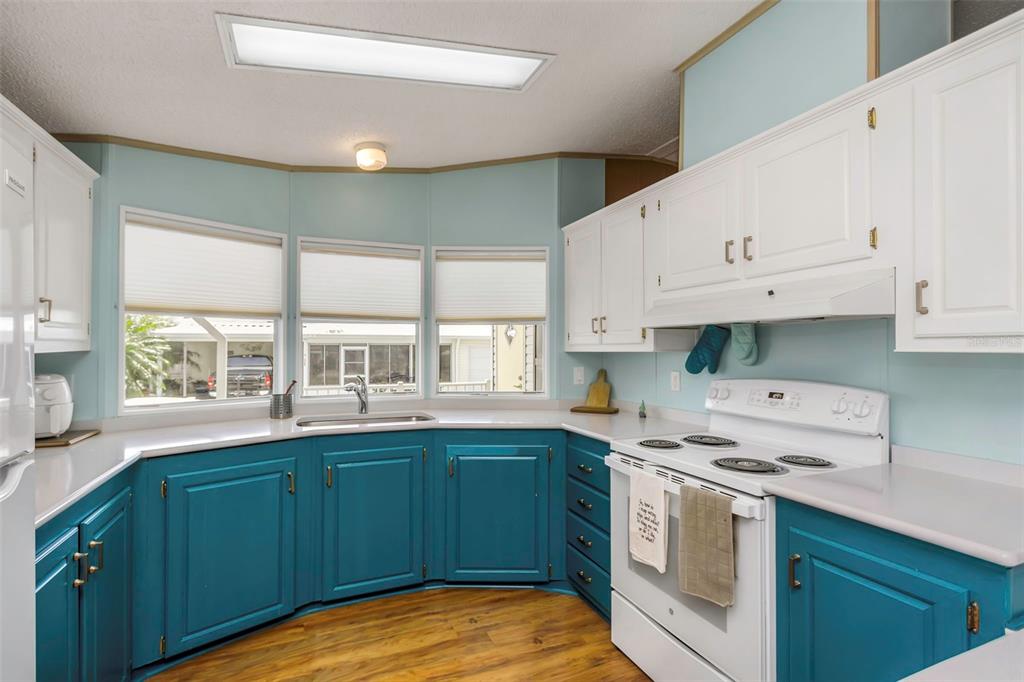 A kitchen features teal lower cabinets, white upper cabinets, white appliances, and a bay window — 106 THATCH PALM STREET W, LARGO, FL