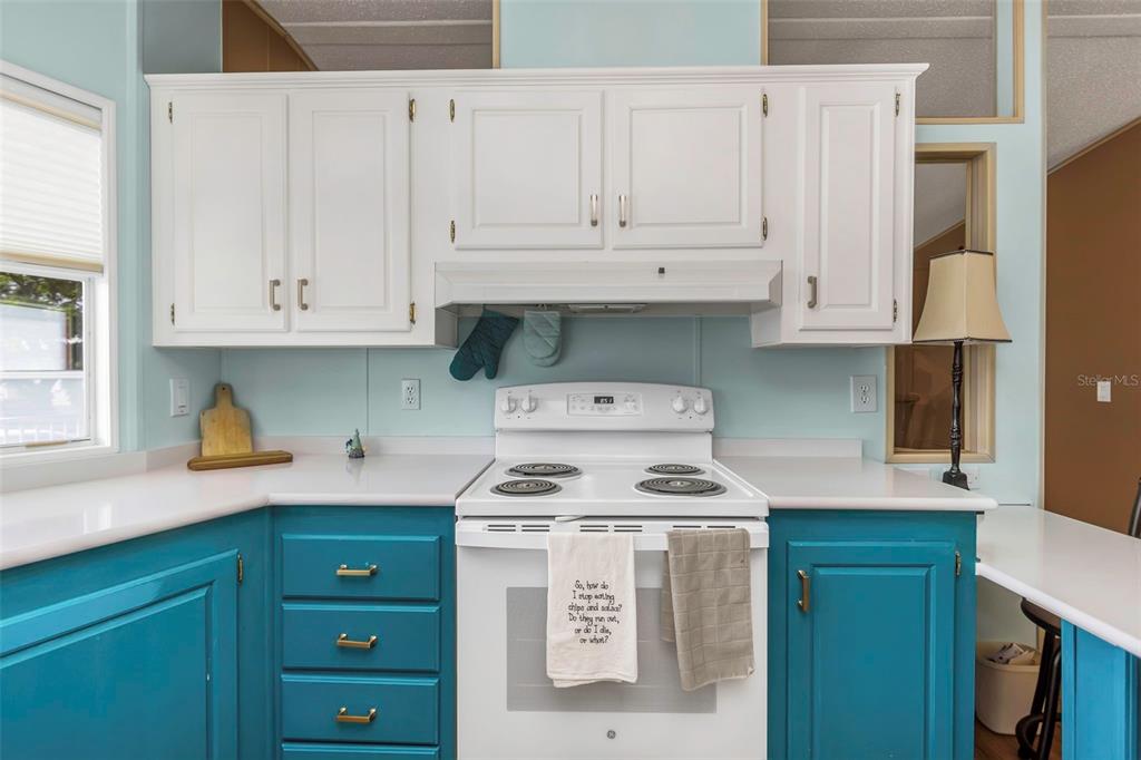 A kitchen features white upper cabinets, teal lower cabinets, a white stove, and light countertops — 106 THATCH PALM STREET W, LARGO, FL