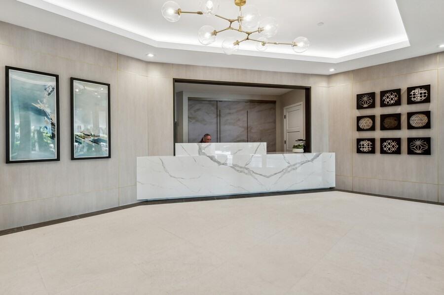A modern reception area features a white marble desk, geometric chandelier, and minimalist wall art — 86 Macfarlane Drive # 8f, Delray Beach FL 33483, DELRAY BEACH, FL