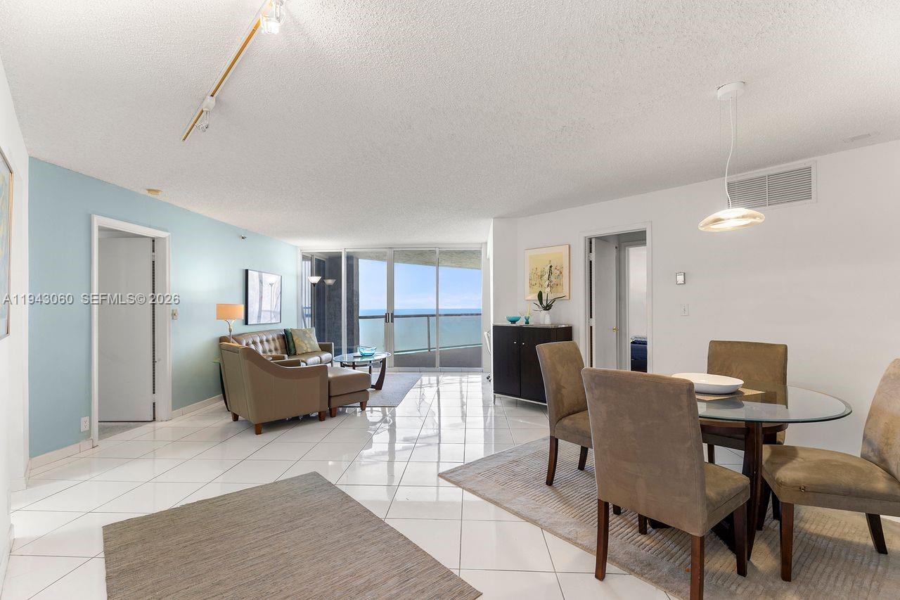 This living and dining area features white tile floors, light blue walls, and a balcony view — 6767 Collins Ave # 1905, Miami Beach FL 33141, MIAMI BEACH, FL