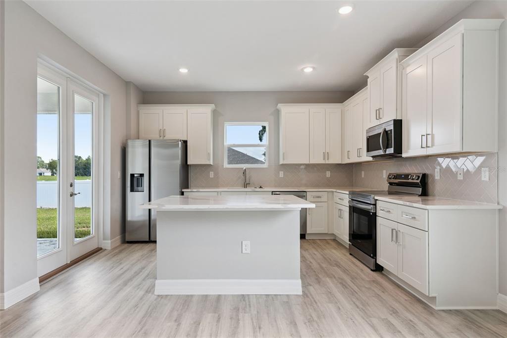 A modern kitchen features white cabinets, stainless steel appliances, a center island, and light flooring — 4843 SW 131ST PLACE, OCALA, FL