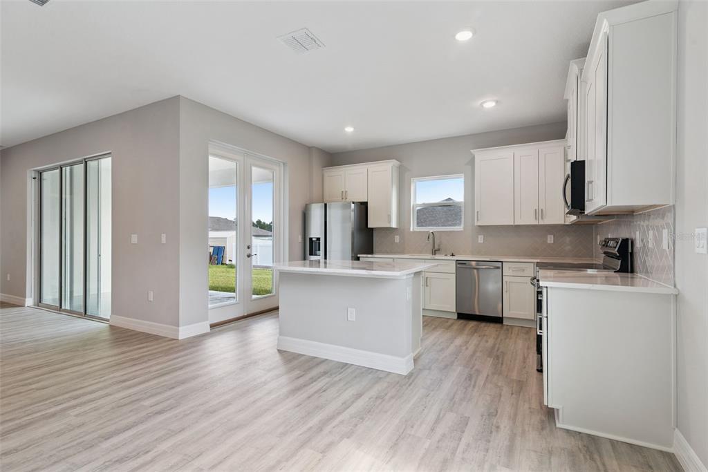 A modern kitchen features white cabinets, stainless steel appliances, an island, and light wood flooring — 4843 SW 131ST PLACE, OCALA, FL