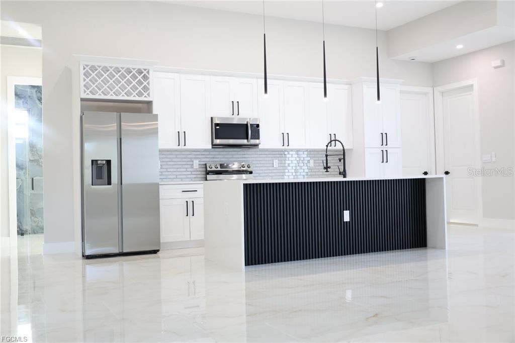 A modern kitchen features white cabinets, stainless steel appliances, and a black slatted kitchen island — 3512 9TH STREET W, LEHIGH ACRES, FL