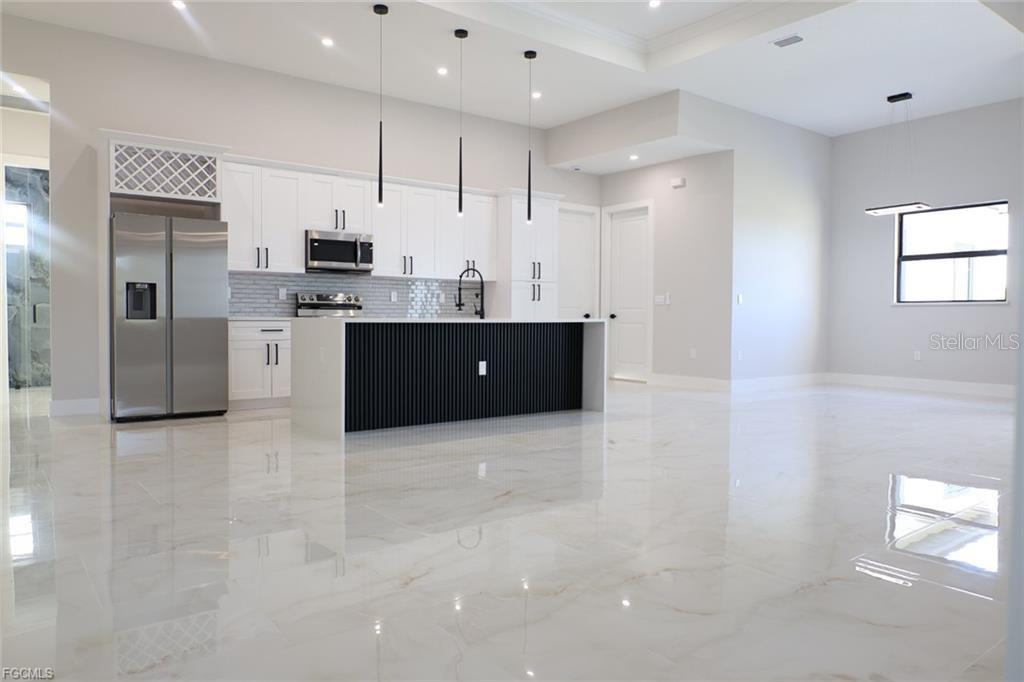 A modern kitchen features white cabinetry, a black slatted island, and polished marble-look flooring — 3512 9TH STREET W, LEHIGH ACRES, FL