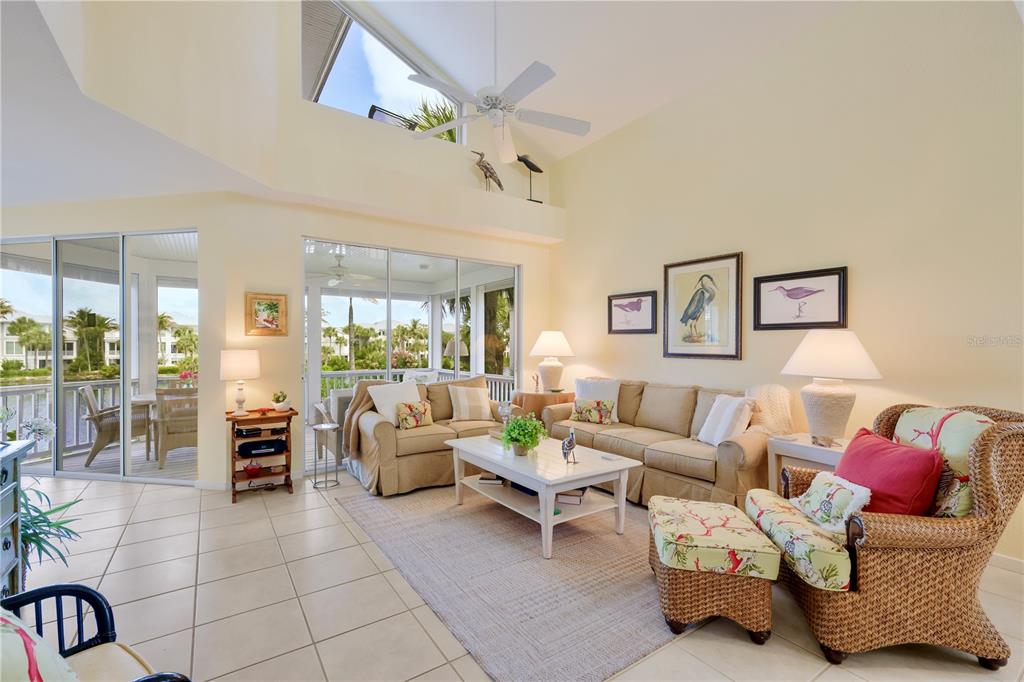 A bright living room features a vaulted ceiling, tile floors, and sliding doors to a patio — 760 SEABOARD LINE LANE, BOCA GRANDE, FL