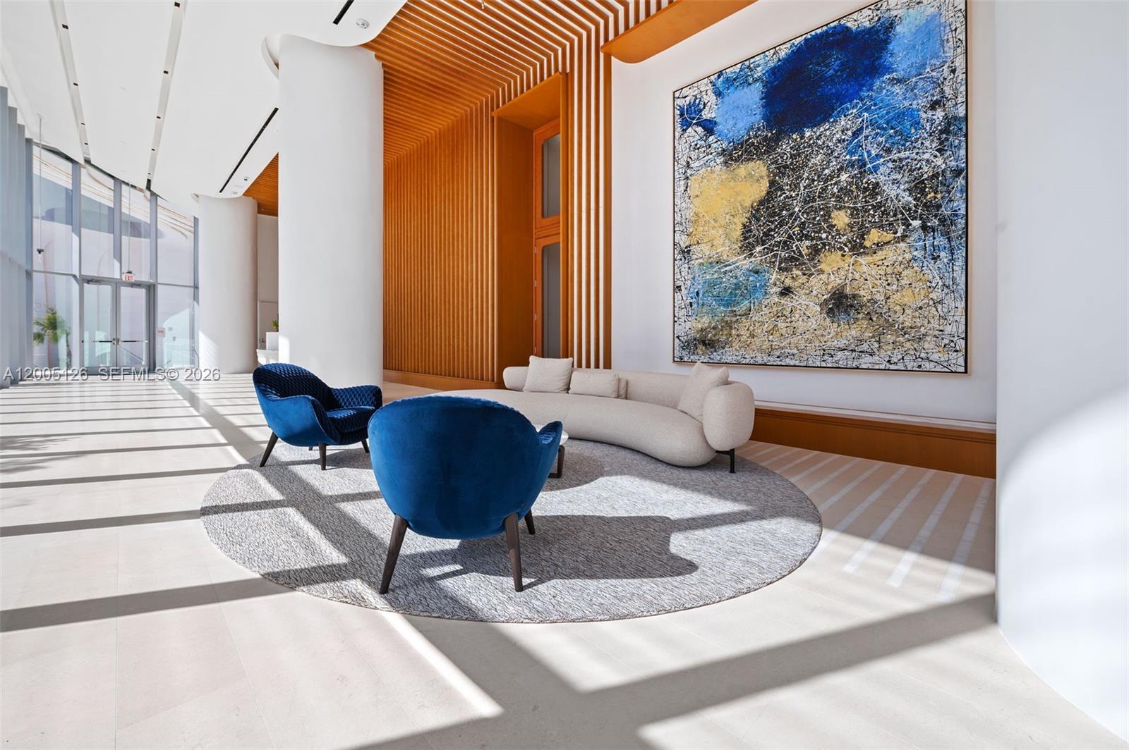 A modern lobby features a curved sofa, two blue armchairs, and a large abstract painting — 175 SE 25 RD # 2604, Miami FL 33129, MIAMI, FL