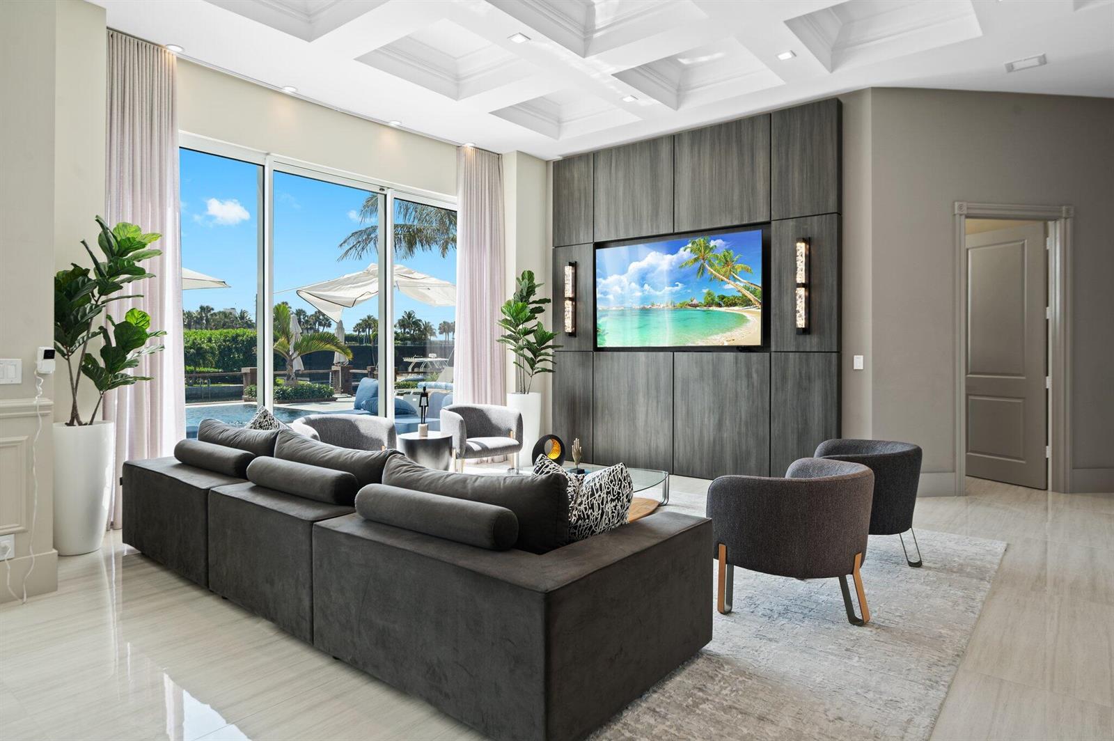 A modern living room features a large gray sectional, a wood-paneled media wall, and floor-to-ceiling windows — 81 S Island Dr, Ocean Ridge FL 33435, OCEAN RIDGE, FL
