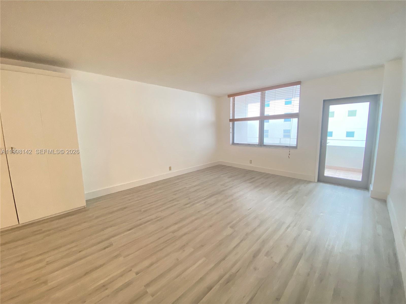 An empty room features light wood-look flooring, a white wardrobe, a window, and a door — 9225 Collins Ave # 706, Surfside FL 33154, SURFSIDE, FL