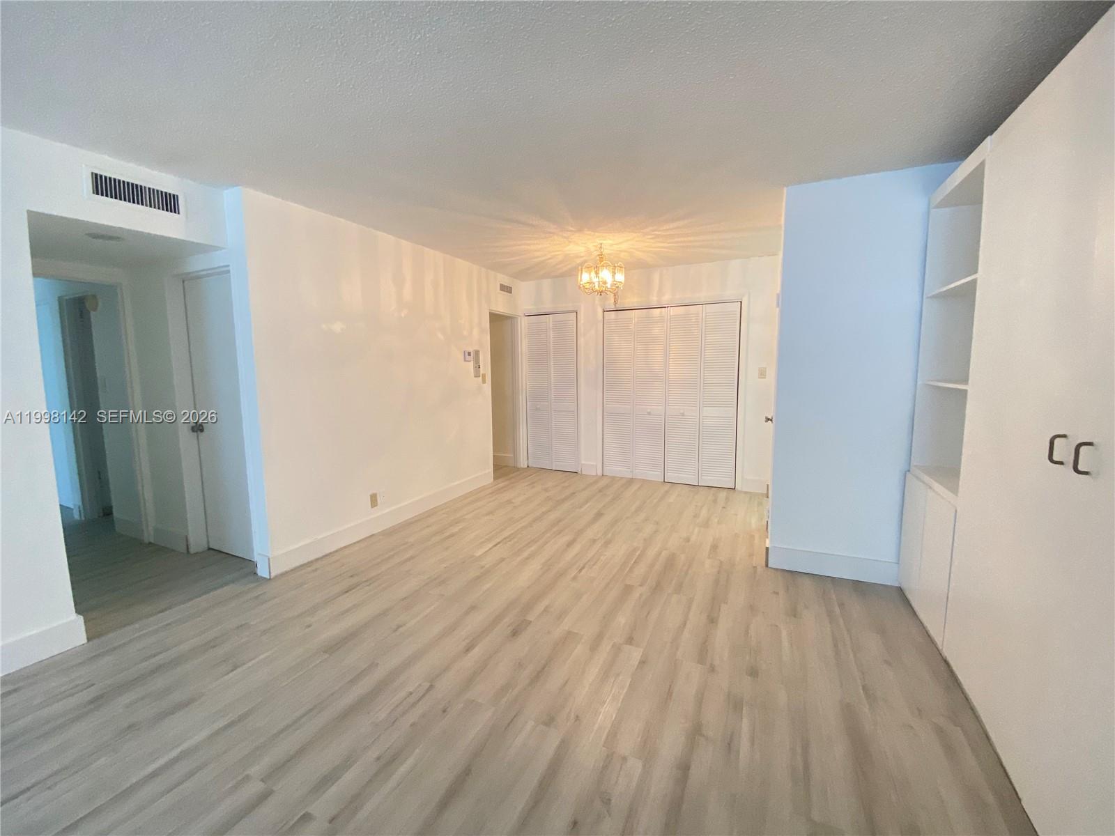 A bright, empty room features light wood-look flooring, white walls, and white louvered closet doors — 9225 Collins Ave # 706, Surfside FL 33154, SURFSIDE, FL