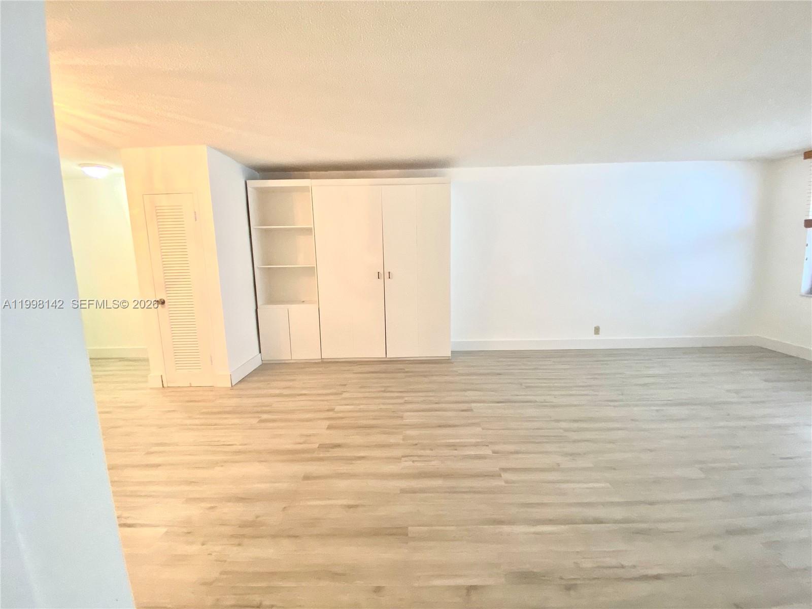 A room with light wood-look flooring, white walls, and a built-in white storage unit — 9225 Collins Ave # 706, Surfside FL 33154, SURFSIDE, FL