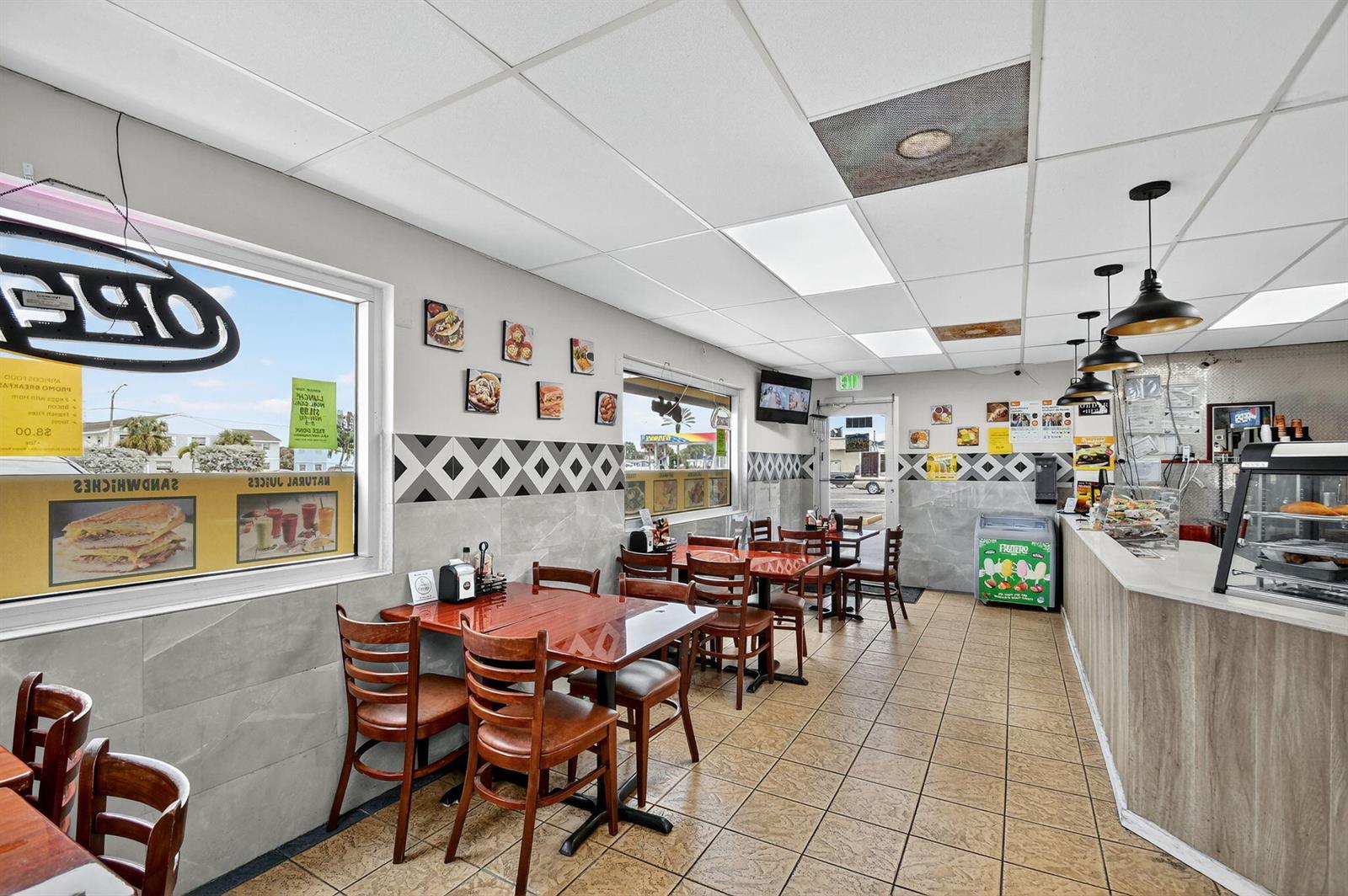 A restaurant interior features wooden tables, chairs, tiled floors, and a service counter — 1541 W Blue Heron Boulevard, Riviera Beach FL 33404, RIVIERA BEACH, FL
