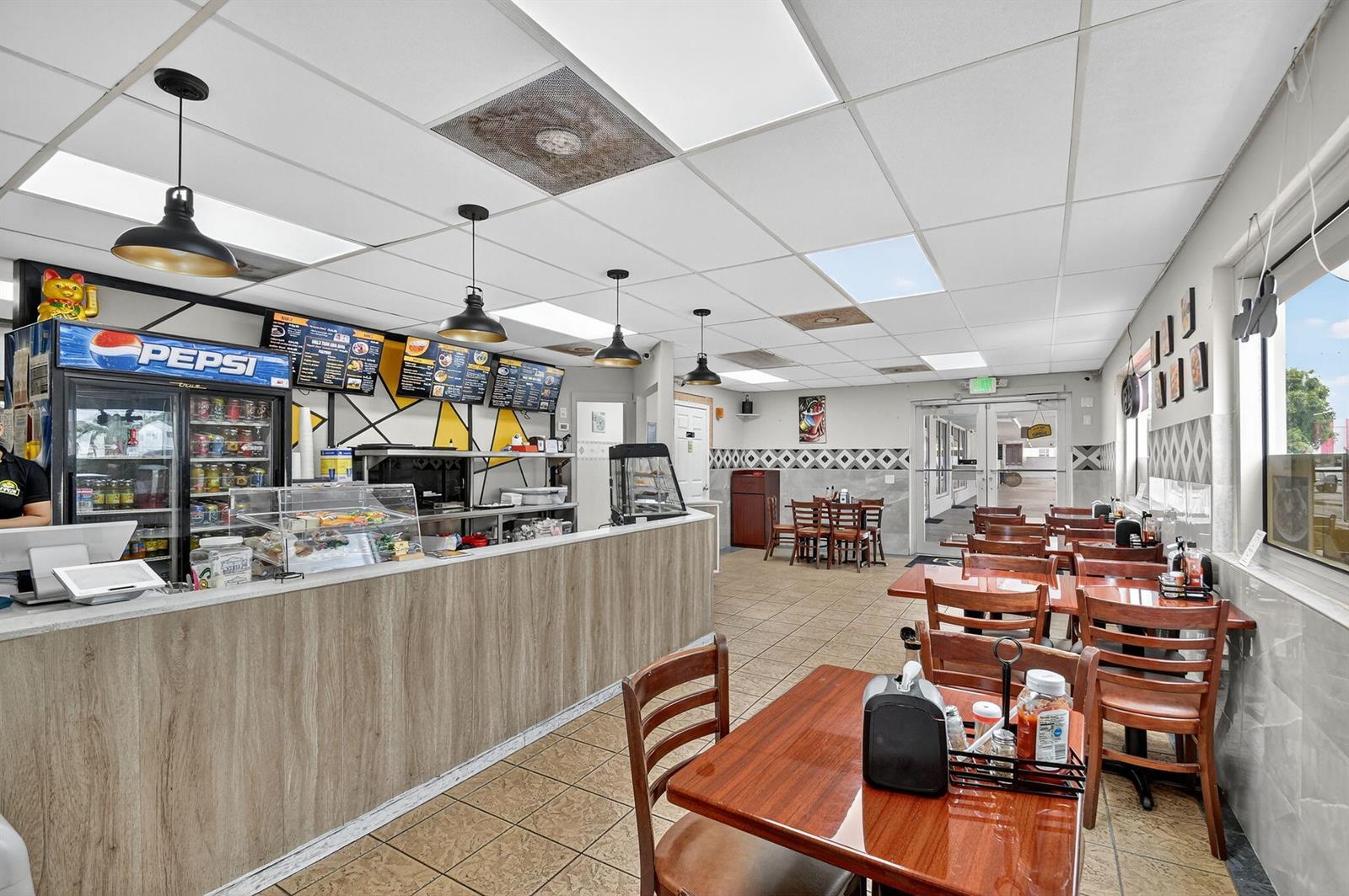 A restaurant interior features a service counter, dining tables, and pendant lighting under a ceiling — 1541 W Blue Heron Boulevard, Riviera Beach FL 33404, RIVIERA BEACH, FL