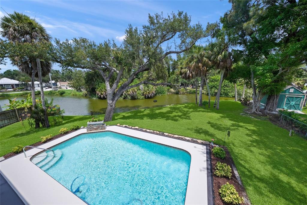 An elevated view of a backyard swimming pool overlooking a pond surrounded by mature trees — 3643 MERIDALE ROAD, SARASOTA, FL