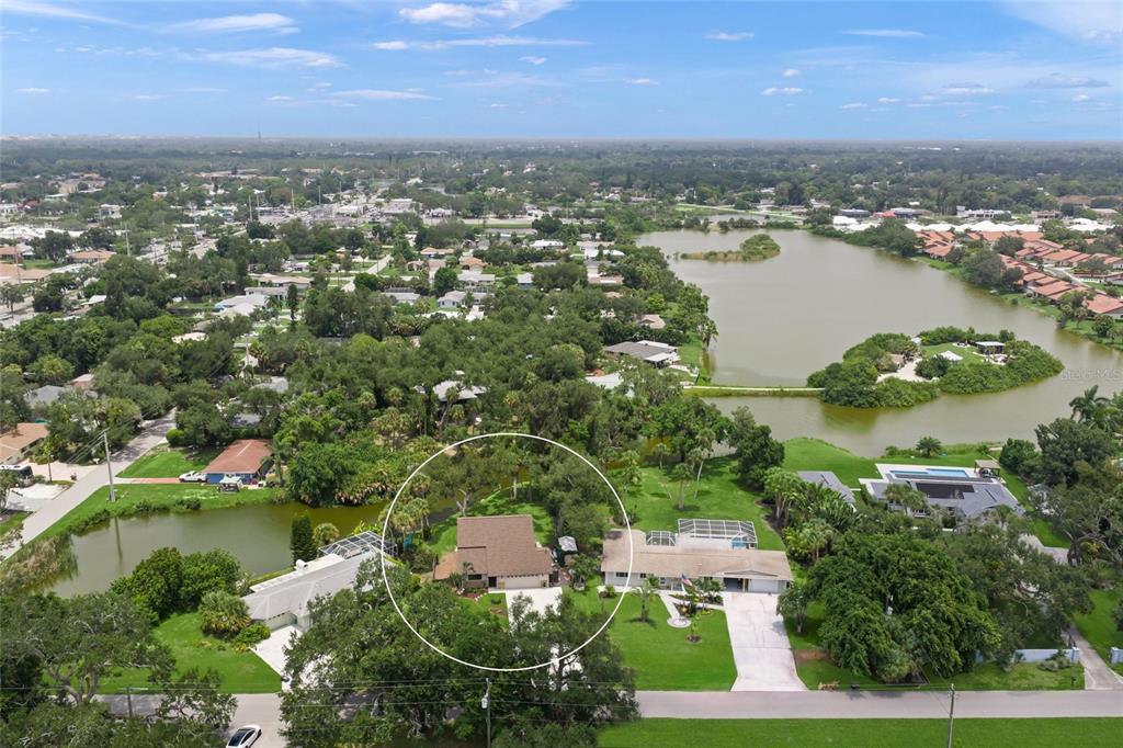 An aerial view shows a residential house circled in a yard with trees and water — 3643 MERIDALE ROAD, SARASOTA, FL