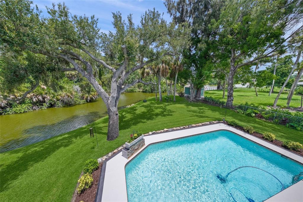 An elevated view of a backyard swimming pool overlooking a canal surrounded by lush trees — 3643 MERIDALE ROAD, SARASOTA, FL