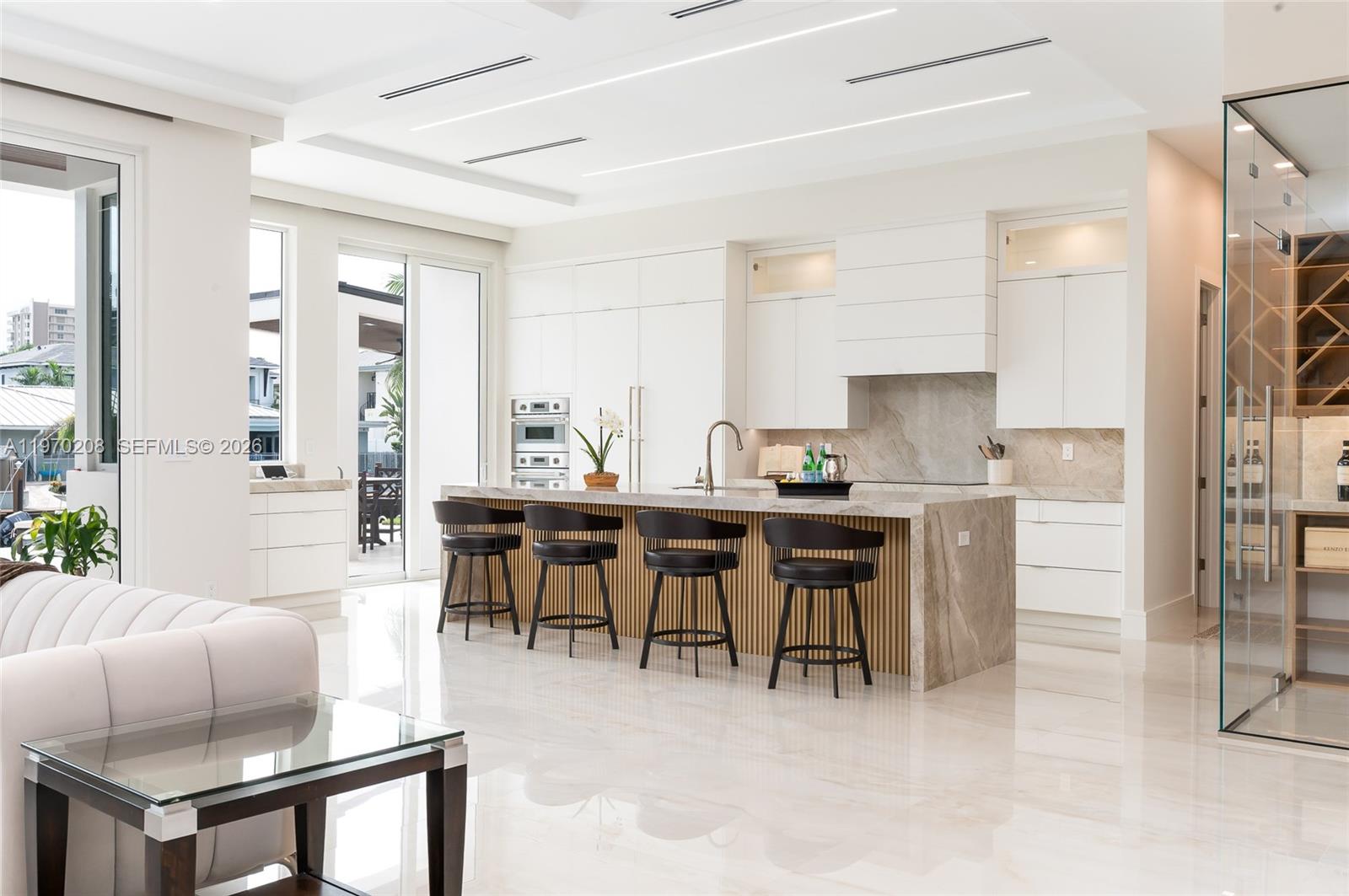 A modern kitchen features a marble island with bar seating and white cabinetry — 3740 NE 29th Ave, Lighthouse Point FL 33064, LIGHTHOUSE POINT, FL