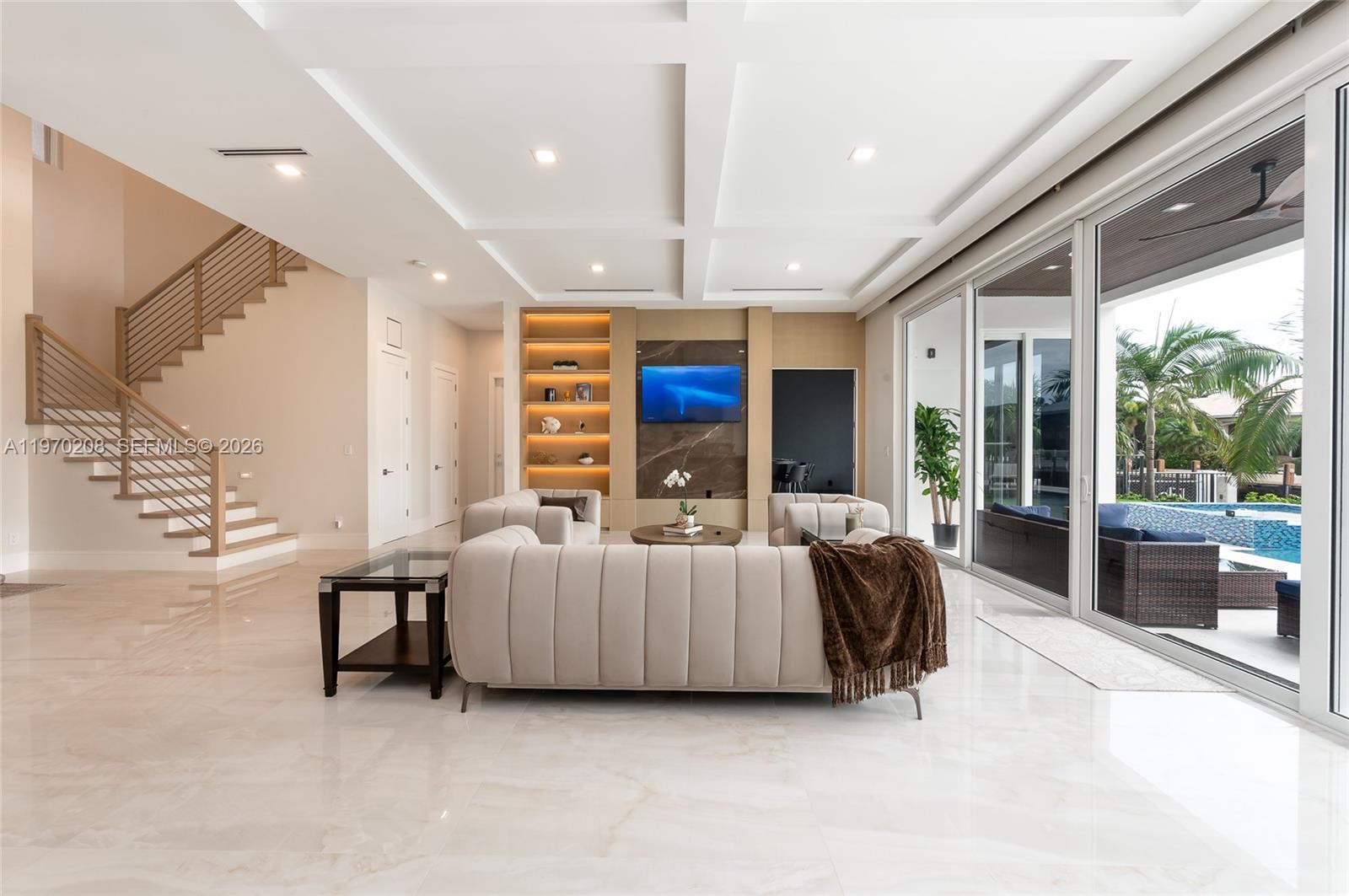 A modern living room features a coffered ceiling, marble floors, and large sliding glass doors — 3740 NE 29th Ave, Lighthouse Point FL 33064, LIGHTHOUSE POINT, FL