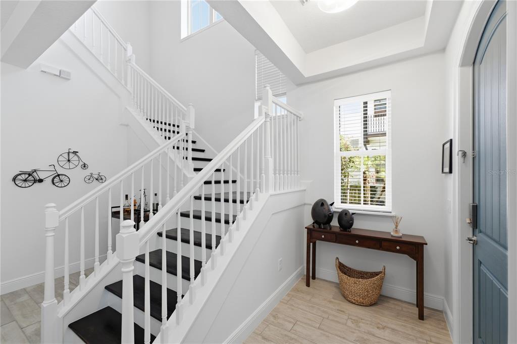An entryway features a staircase with dark treads, white railings, and a wooden console table — 8873 FOUNTAIN PALM ALLEY, WINTER GARDEN, FL