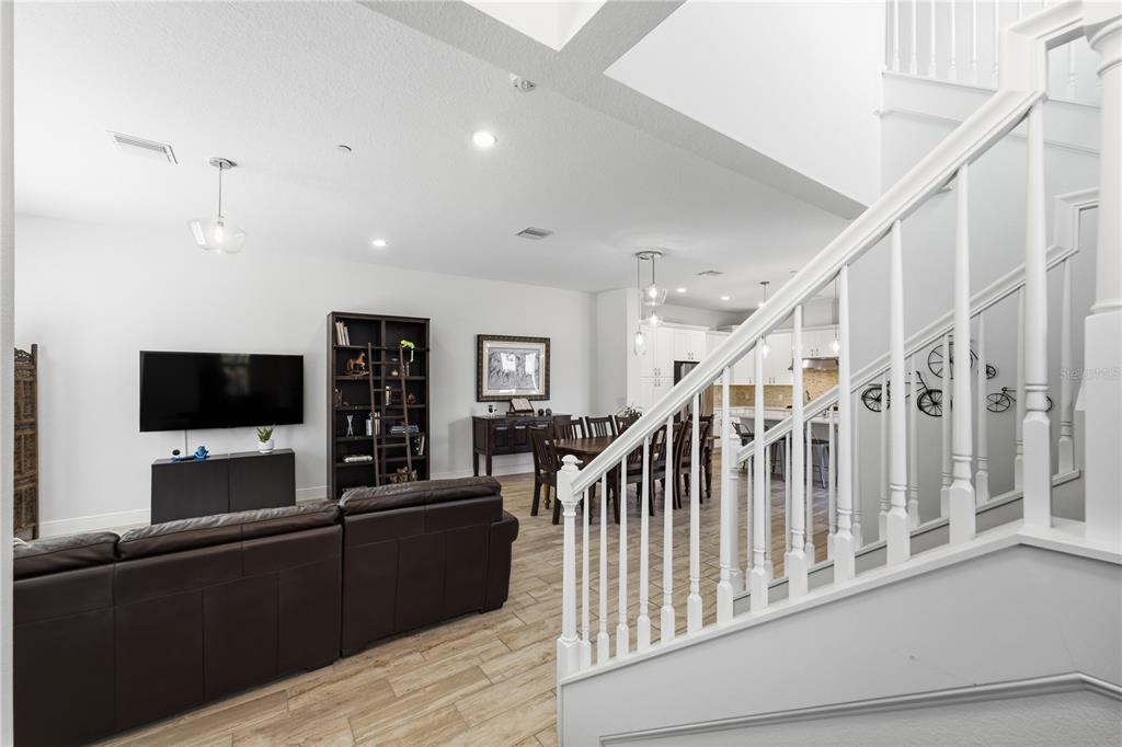 A living room with a brown leather sofa, television, bookshelf, and a staircase leading upstairs — 8873 FOUNTAIN PALM ALLEY, WINTER GARDEN, FL