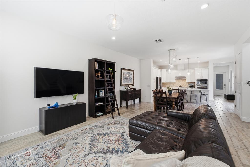 An open-concept living room features a dark leather sectional, a bookshelf, and a dining area — 8873 FOUNTAIN PALM ALLEY, WINTER GARDEN, FL