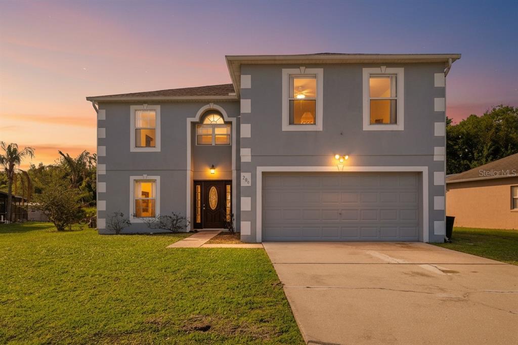 A two-story gray house with white trim and a two-car garage at sunset — 206 TARANTO WAY, KISSIMMEE, FL