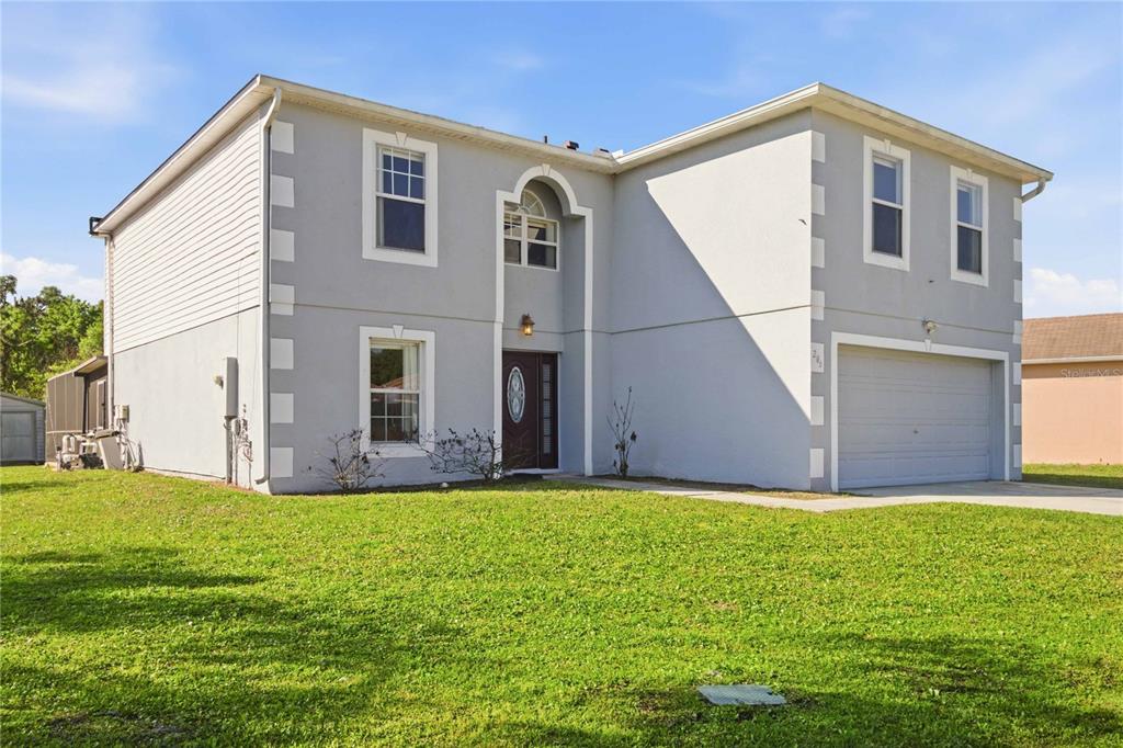 A two-story house with a gray stucco exterior, a front-facing garage, and a lawn — 206 TARANTO WAY, KISSIMMEE, FL