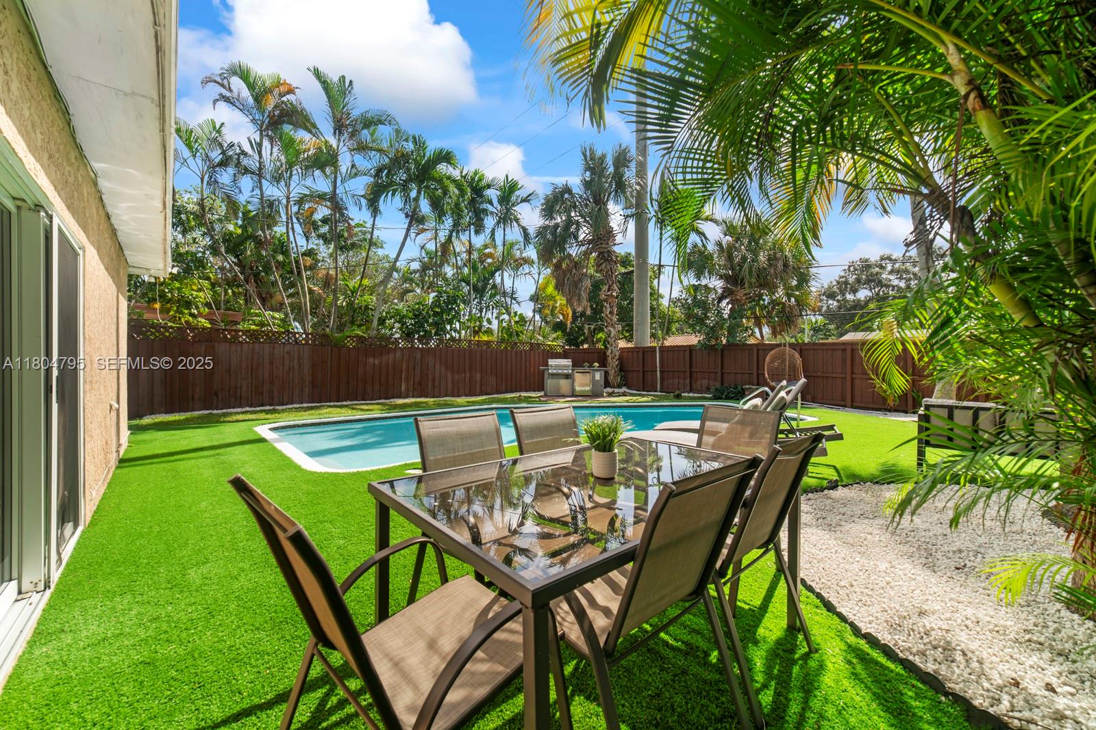 A backyard features a swimming pool, a dining set on artificial turf, and palm trees — 2708 Cleveland St, Hollywood FL 33020, HOLLYWOOD, FL