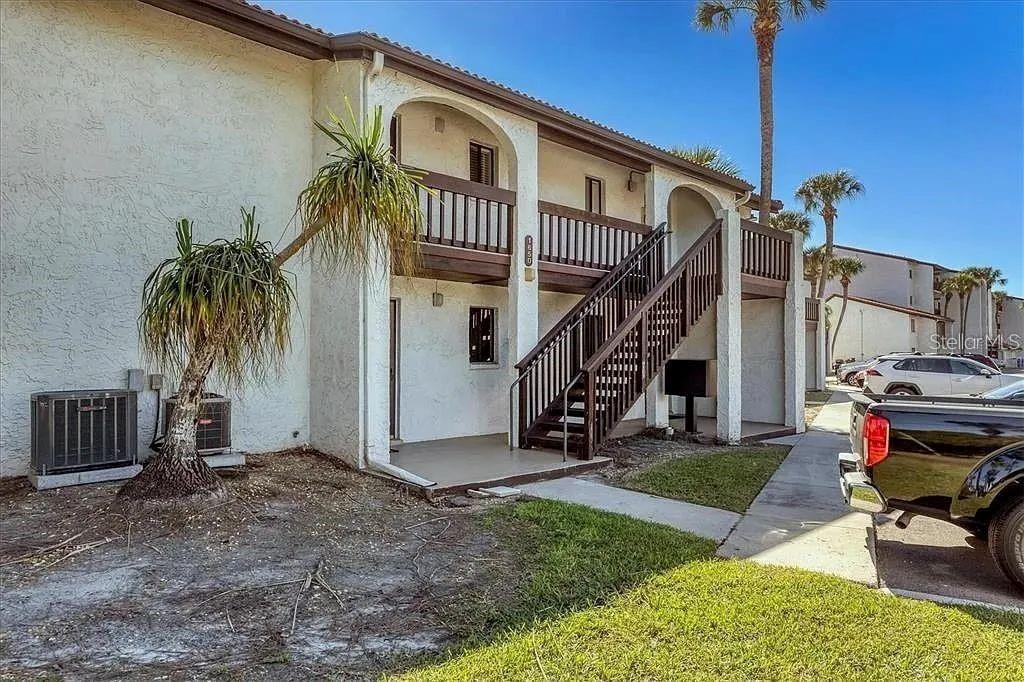 A two-story apartment building features a wooden staircase, arched balconies, and a palm tree — 1650 STICKNEY POINT ROAD UNIT 50-202, SARASOTA, FL