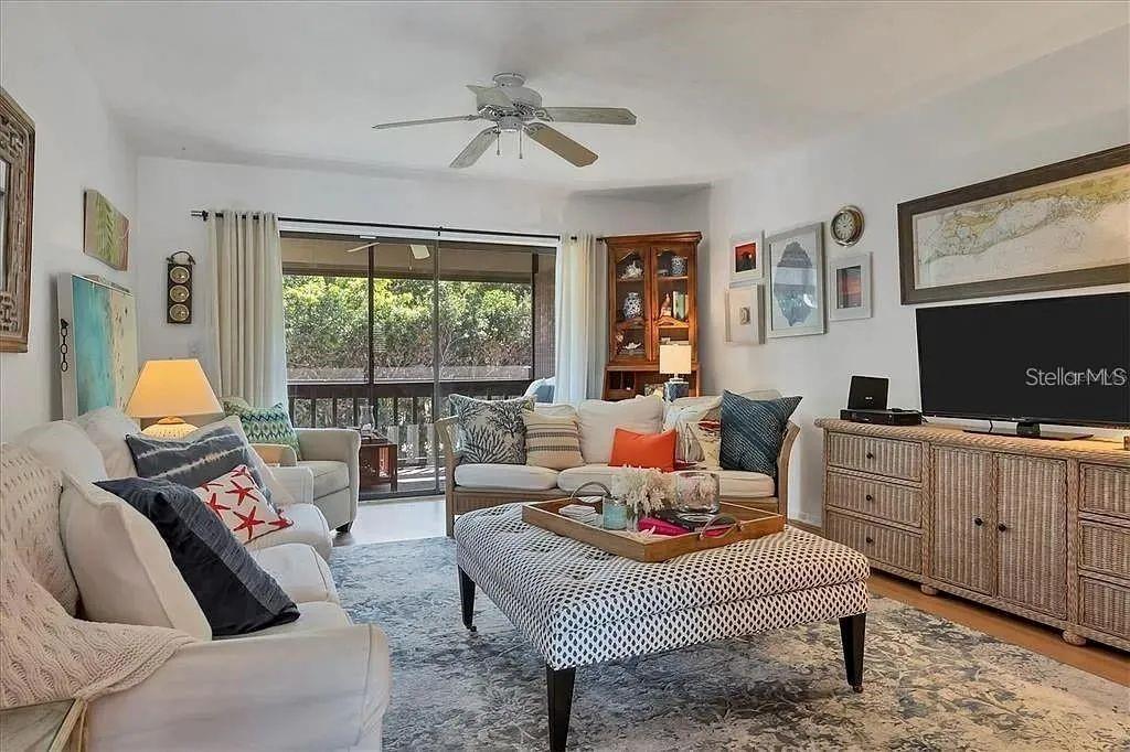 A living room features white sofas, a patterned ottoman, and a large television on a console — 1650 STICKNEY POINT ROAD UNIT 50-202, SARASOTA, FL